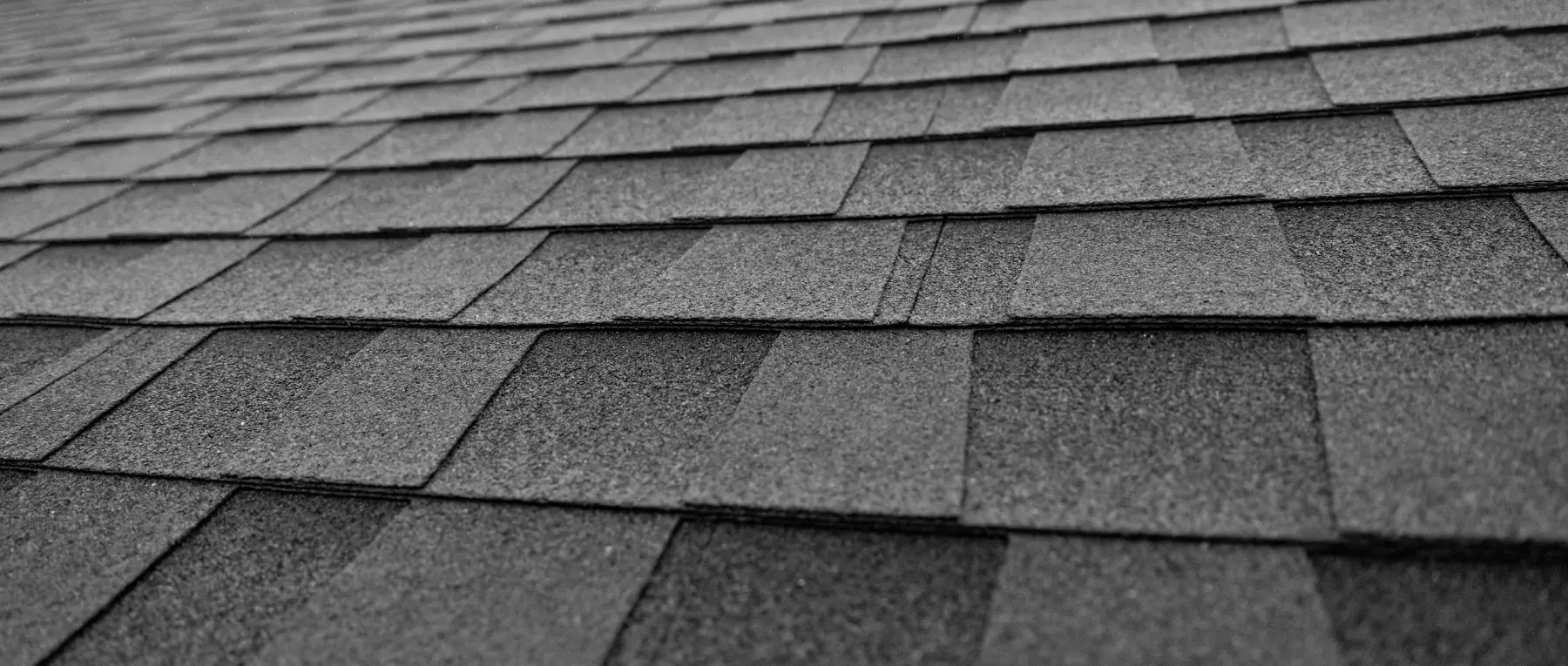 Close-up view of overlapping rows of gray asphalt roof shingles, creating a textured pattern across the roof surface.