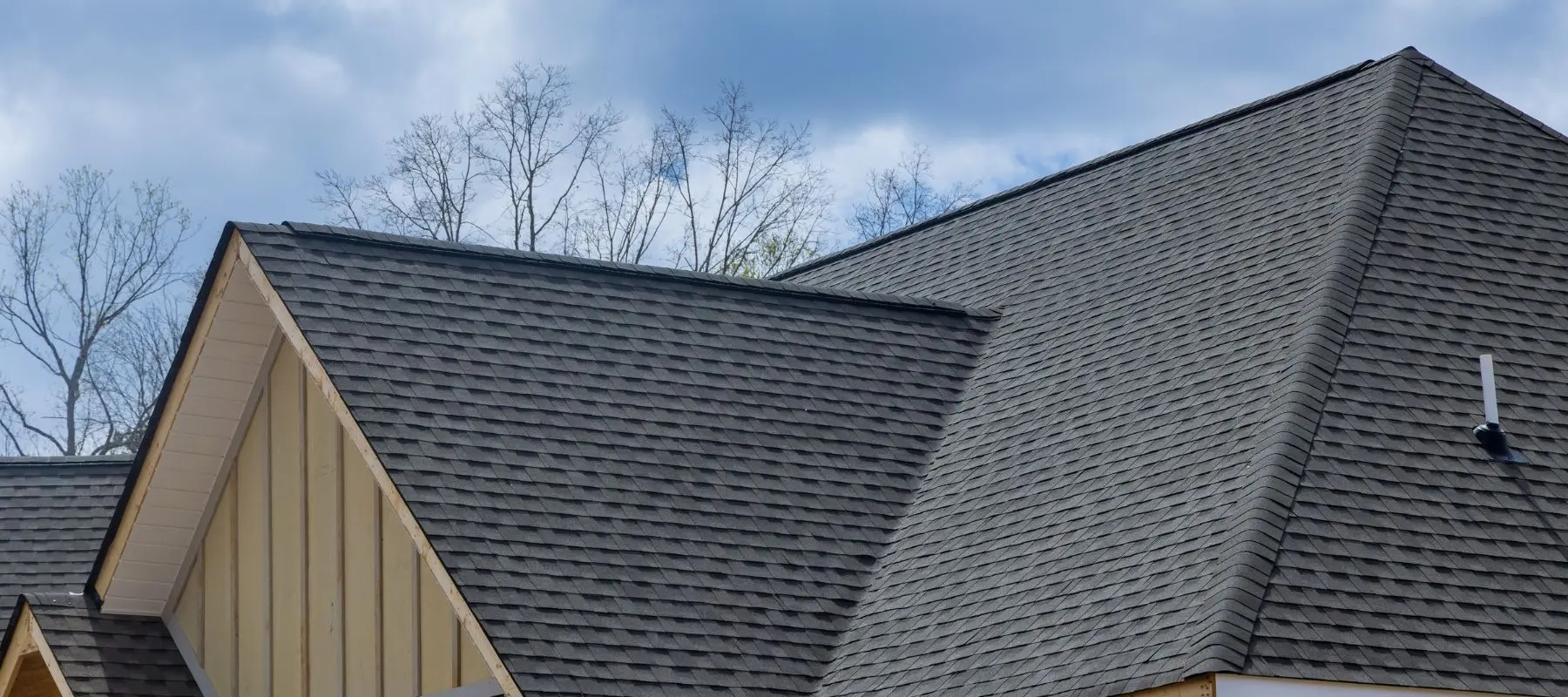 A close-up view of a newly installed dark shingle roof on a house with tan vertical siding.