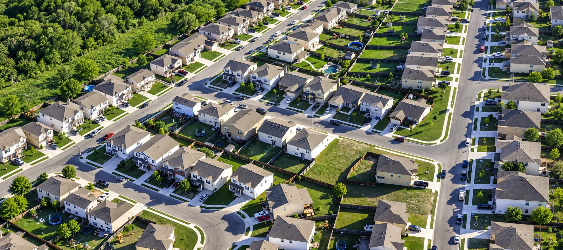 Aerial view of a suburban neighborhood with many detached houses, paved streets, and green lawns.
